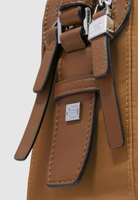 Braune Ledertasche mit Details, die eine glatte Textur, mehrere Riemen, silberne Beschläge und ein quadratisches Logo-Akzent zeigen.