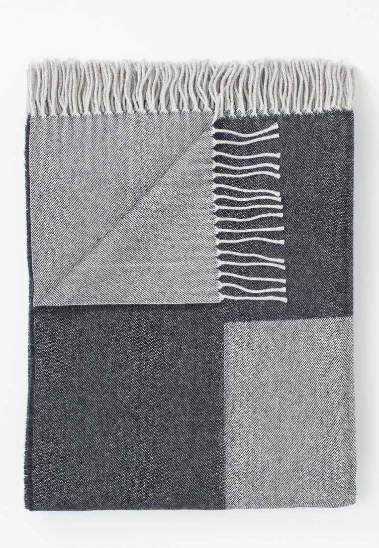 Wollene Decke gefaltet mit grau und dunkelgrau diagonalen Streifen und fransigen Kanten auf einem weißen Hintergrund.