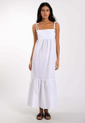 Vestido maxi blanco sin mangas con escote cuadrado, tejido texturizado, dobladillo en capas y tirantes ajustables con lazo. Combinado con sandalias negras de tiras.