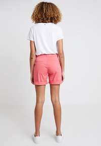 Różowe szorty z wywiniętymi mankietami i tylnymi kieszeniami, połączone z białą koszulką. Tkanina wydaje się gładka i ma lekką teksturę.