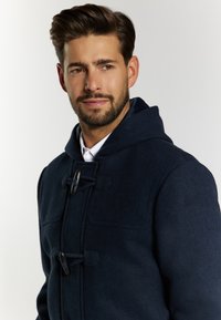 Sötétkék gyapjú duffle kabát kapucnival, kerek gombokkal, két elülső zsebbel és texturált felülettel.