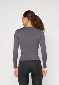 Dolga majica z dolgimi rokavi, izrazito oprijetega kroja iz temno sive tkanine, gladke teksture, s krožnim izrezom in brezšivnimi manšetami, v kombinaciji z črnimi legginsi.
