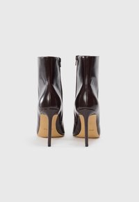 Botine din piele maro, cu o textură netedă, toc înalt de tip stiletto și fermoar lateral pentru acces ușor.