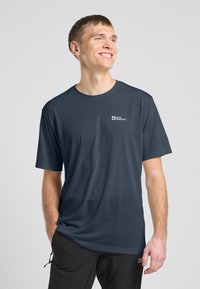 Chemise à manches courtes bleu foncé avec une coupe décontractée et une texture lisse, présentant un petit logo blanc sur la poitrine et un design minimaliste.