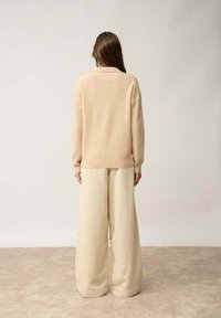 Pull en maille beige avec col, associé à un pantalon large en ribby beige clair. La texture et la couleur créent une tenue douce et neutre.