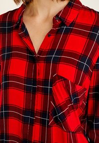 Rød ternet button-up skjorte med en lomme, kontrasterende sorte og hvide linjer, letvægtigt stof og krave.
