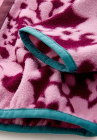 Rózsaszín polár takaró lila absztrakt mintákkal. A szélén tengerzöld szegéllyel. Puha textúra, hajtásának rétegzett mintája látható.