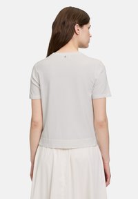 Jasnoszara koszulka z krótkim rękawem, okrągłym dekoltem i prostym wykończeniem. Wykonana z miękkiego materiału, z małym detalem logo blisko tylnego dekoltu.
