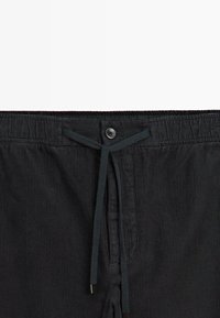 Zwarte corduroy shorts met een gestructureerd streepmotief, voorzien van een elastische tailleband, een knoopsluiting en een trekkoord.
