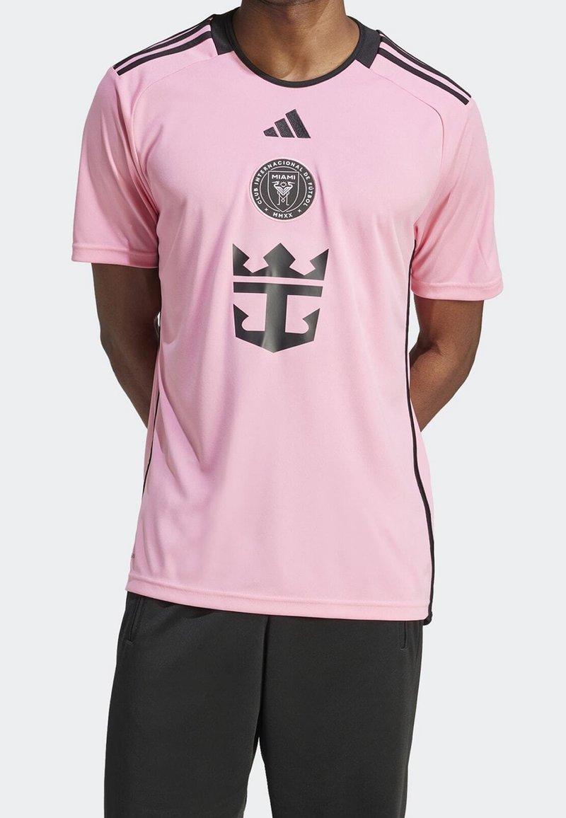 Mann trägt rosa Inter Miami Fußballtrikot mit schwarzem Adidas-Logo, Vereinswappen und großem schwarzem Kronenemblem auf der Vorderseite.