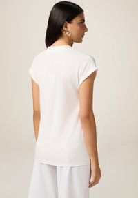 Top bianco a maniche corte realizzato in tessuto leggero. Presenta un scollatura rotonda e maniche arrotolate. Design semplice e pulito.