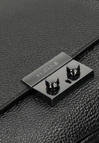 Czarna torebka z fakturowanej skóry z błyszczącym czarnym metalowym zapięciem z dwoma okrągłymi przyciskami oraz wygrawerowanym logo marki "wojas."