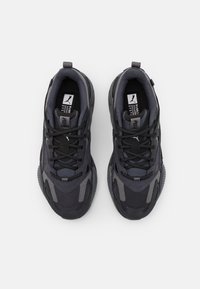 Chaussures de sport noires et grises avec tissu texturé, accents en mesh, et système de laçage proéminent. Dotées d'un logo sur la languette et d'un col rembourré.