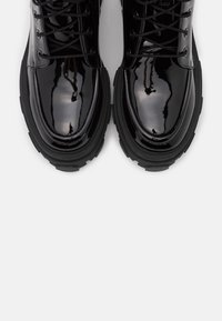 Bottes à lacets en cuir noir brillant avec semelles épaisses en caoutchouc, vues de dessus sur un fond blanc.