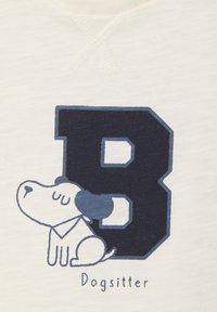 Weißes Stoffhemd mit einem großen marineblauen "B" und einem im Profil dargestellten Cartoon-Hund, begleitet von dem Text "Dogsitter" darunter.