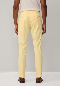 Lys gule chinos med slim fit, der har to baglommer fastgjort med knapper og opfoldede nederste kanter, parret med brune sko.