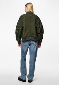Casaco bomber verde-azeitona com mangas franzidas, bainha e colarinho canelados; combinado com jeans de perna larga azul-claro. Design simples e textura suave.