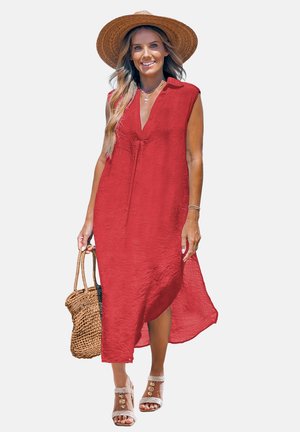 Frau trägt ein ärmelloses rotes Midikleid, Strohhut, beige Sandalen mit Absatz, hält eine geflochtene Strohtasche, lächelt und geht nach vorne.