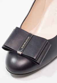 Scarpa flat in pelle blu navy con un grande fiocco in satin, caratterizzata da un dettagli metallici del logo. Punta tonda e superficie liscia.