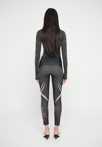 Svarte leggings med rosa og hvite diagonale detaljer, høy midje og en elastisk, glatt tekstur. Langermet grønn topp kompletterer antrekket.