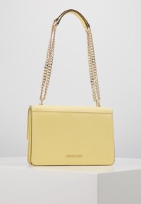 Gul læder crossbody taske med en rektangulær form, der har en kædesnor og en præget mærkelogo på forsiden.