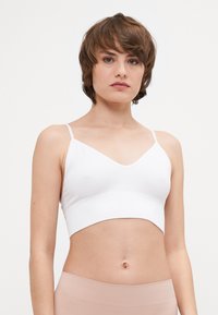Vit ribbad bralette med V-ringning och tunna justerbara axelremmar. Slät textur och kort design, i kombination med ljusbeige underdelar.