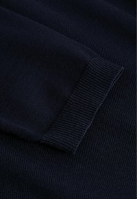 Mørkeblå strikket stof med et nærbillede af en ribbet manchet-sektion, der viser detaljeret tekstur og syningsmønstre.