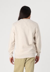Beige genser med lange ermer, ribbestrikkede mansjetter og kant. Har rund hals og et glatt, litt teksturert stoff.