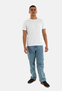 Witte t-shirt met korte mouwen en een ronde hals, gecombineerd met lichtblauwe denim jeans en zwarte schoenen met bruine accenten.