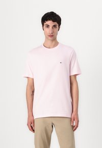 T-shirt en coton rose clair avec un col rond et des manches courtes, arborant un petit logo brodé sur la poitrine et une coupe décontractée.