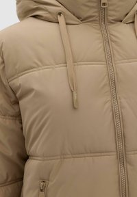 Beige pufferjakke med hætte, fremhævet af en frontlynlås og snor, kviltet design og glat tekstur.
