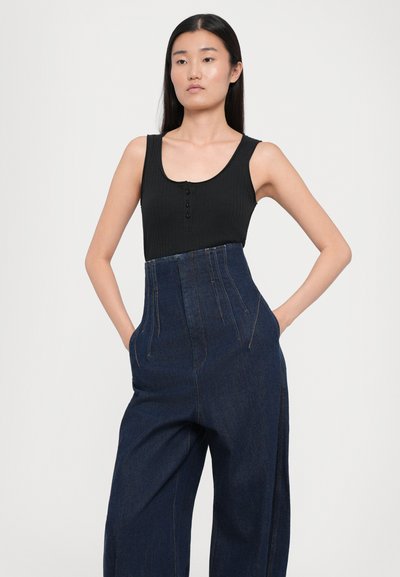 Top cu bretele negre, cu dungă, și butoane, asortat cu pantaloni din denim cu talie înaltă. Pantalonii au un croi larg la picioare și detalii subtile de cusătură.