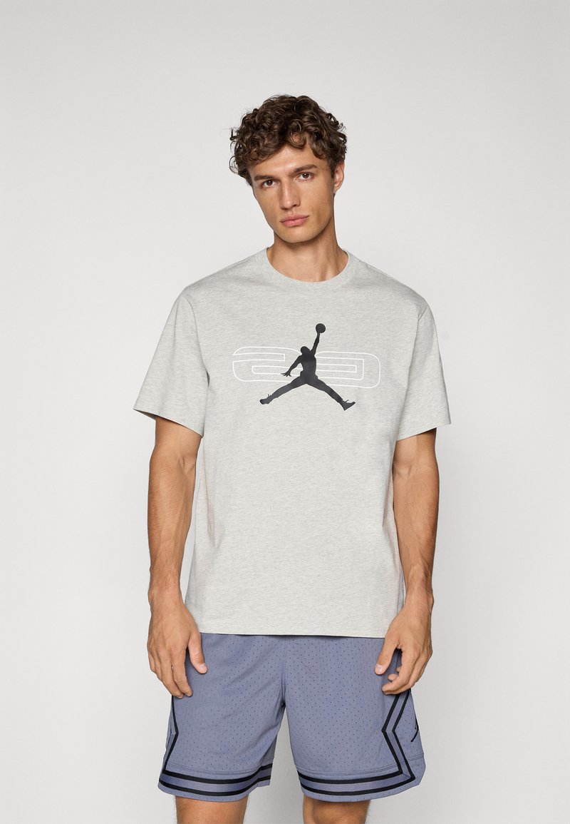 Camiseta gris de algodón con mangas cortas y cuello redondo, que presenta un gráfico del logo negro de Jordan en la parte delantera.
