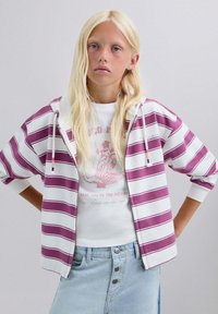 Sudadera con capucha y cremallera con rayas granate y blancas, combinada con una camiseta gráfica blanca y una falda de mezclilla azul claro, con detalles de botones.