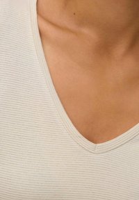 Ljusbeige T-shirt med V-ringning i ribbat tyg med en mjuk struktur, med en subtil glans längs halsringningen och kroppen.