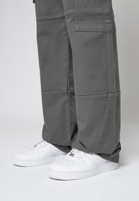 Grijze cargobroek met grote zijzakken en versterkte stiksels, gecombineerd met witte sneakers met een gladde leren textuur en geperforeerde details.