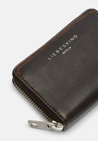 Cartera de cuero marrón con acabado texturizado, con herrajes plateados y una cremallera suave. Logo grabado en el frente.