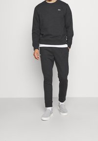 Kolkgrå sweatshirt och matchande joggers med ribbade manchetter, med en liten grön logotyp. Bärs med ljusgrå slip-on skor.