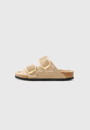 Beige schuifsandalen hebben twee gespen, een voering van bont en een gestructureerde kurken zool, met een zacht suède materiaal en een ronde teenontwerp.