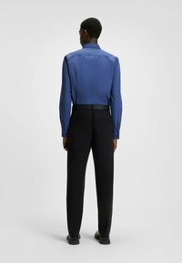 Camicia blu a maniche lunghe con colletto, tessuto morbido, abbinata a pantaloni neri con cintura logo e taglio dritto.