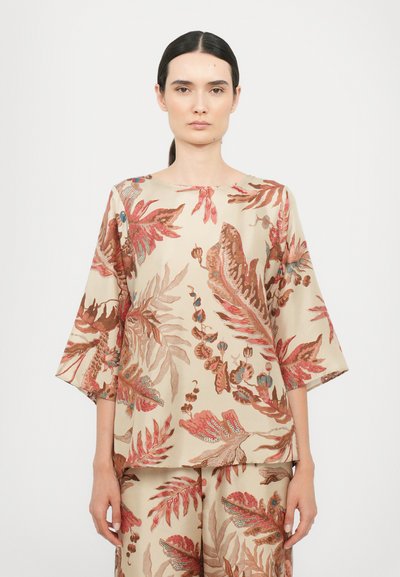 Blouse de couleur crème avec des motifs floraux prononcés en rouge, rose et bleu. Présente une coupe décontractée et des manches de longueur mi-silhouette.
