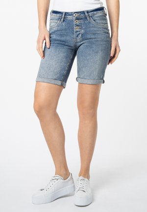 Jeansshorts in verblasstem Hellblau mit einer Fünf-Knopf-Frontschließe, aufgerollten Säumen und Vorder-/Rücktaschen, kombiniert mit weißen Sneakers.