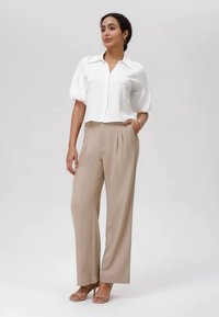 Camicia bianca a maniche corte con texture abbinata a pantaloni beige a vita alta con pince e sandali chiari. Design semplice ed elegante.