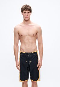 Černé plavecké šortky se žlutými akcenty a bílými bočními panely. Mají šňůrku v pase a volný střih. Vyrobené z odolného syntetického materiálu.