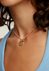 Collar de plata con un charm texturizado, montado en una cadena de cuentas rosa. Las cuentas varían en tamaño, creando un efecto delicado y en capas.