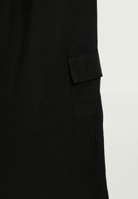 Pantalon cargo noir en coton, avec une poche latérale à rabat, texture lisse et coupe droite.