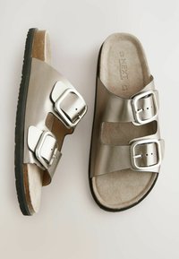 Metalliska silverfärgade slidesandaler med två justerbara silverknäppen, mjuk beige fotbädd och svart texturerad sula för grepp.