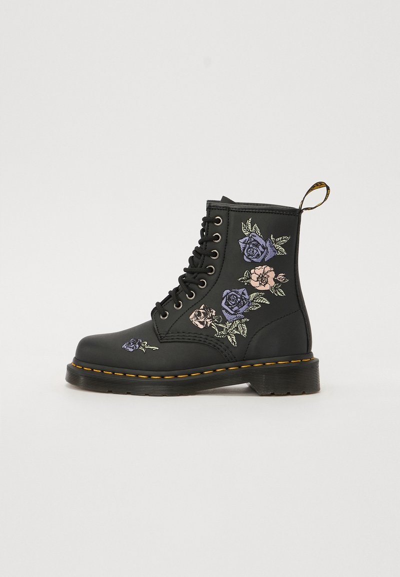 Botte noire à lacets avec couture jaune, ornée de roses brodées en violet, rose et beige, ainsi que de feuilles vertes sur le côté et l'avant.