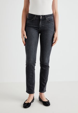 Jeans en denim gris avec une coupe ajustée, taille mi-haute, style à cinq poches et détails de couture subtils. Portés avec des ballerines noires.