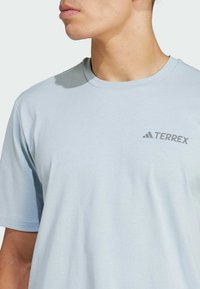 Svetlomodré bavlnené tričko s krátkymi rukávmi, okrúhlym výstrihom a šedým logom "TERREX" potlačeným na ľavej strane hrudníka. Hladká textura.